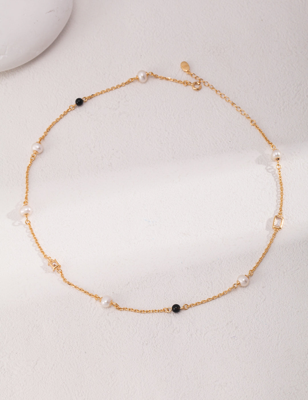 Éclat necklace in 925 sterling silver with natural pearls, black agate, and zircon accents, finished in vintage gold. Adjustable chain length 38cm + 6cm extension, featuring 5.7mm pearls, 4mm agate, and 7mm x 4.8mm zircon for a sophisticated look.