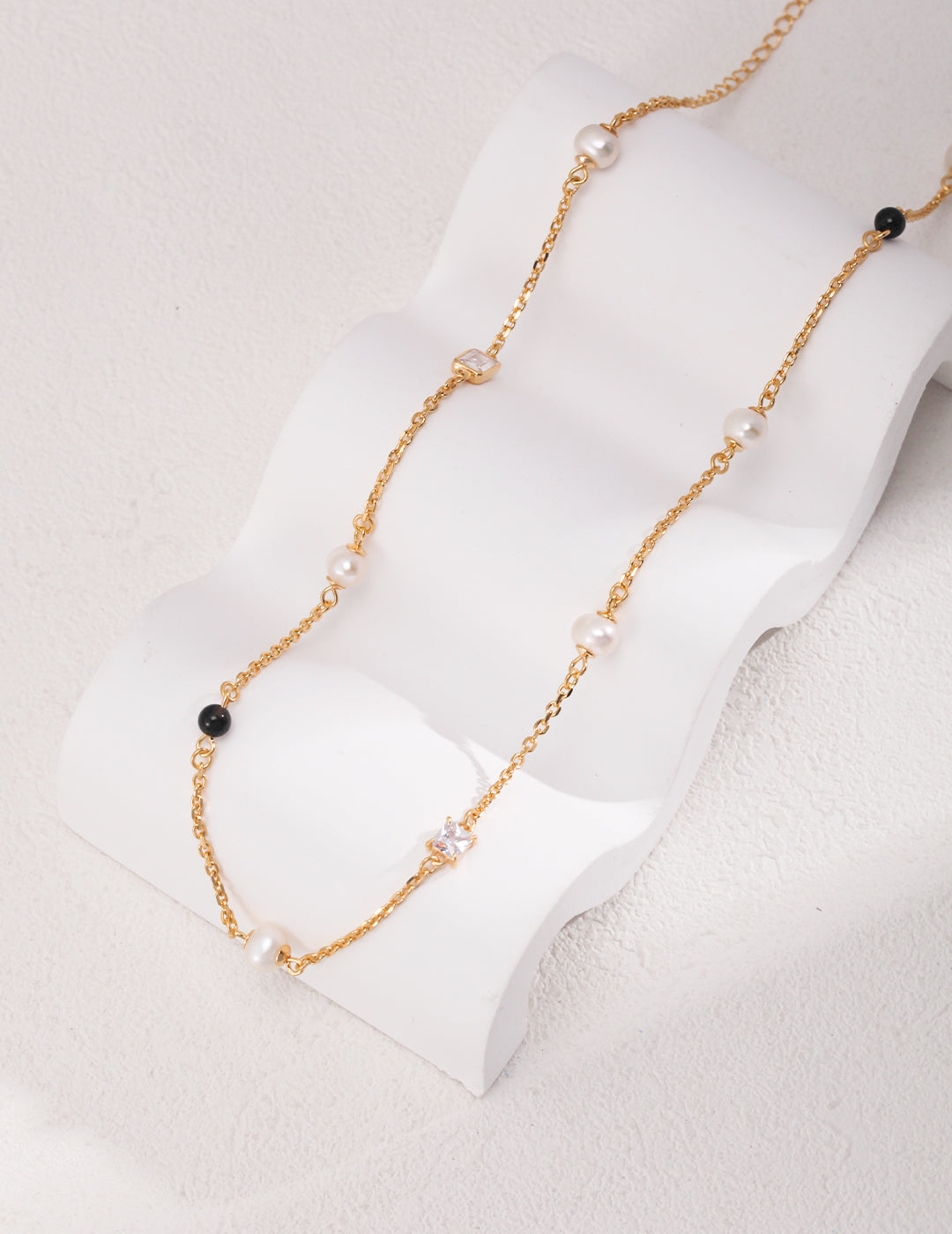 Éclat necklace in 925 sterling silver with natural pearls, black agate, and zircon accents, finished in vintage gold. Adjustable chain length 38cm + 6cm extension, featuring 5.7mm pearls, 4mm agate, and 7mm x 4.8mm zircon for a sophisticated look.